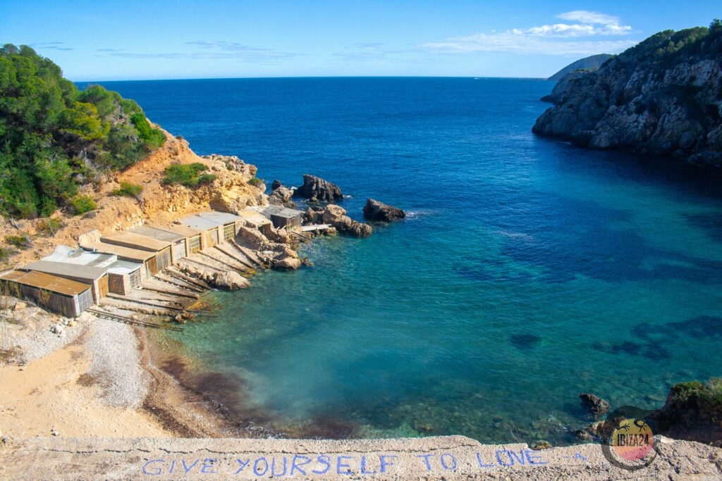 Old fishermen huts at Cala d’en Serra in Ibiza, rustic structures along the rocky beach, surrounded by crystal-clear waters