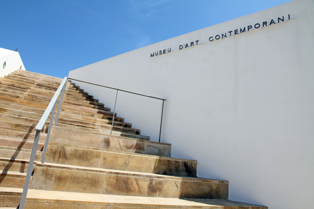 Modern glass extension of MACE juxtaposed with historic stone walls in Ibiza's Dalt Vila.